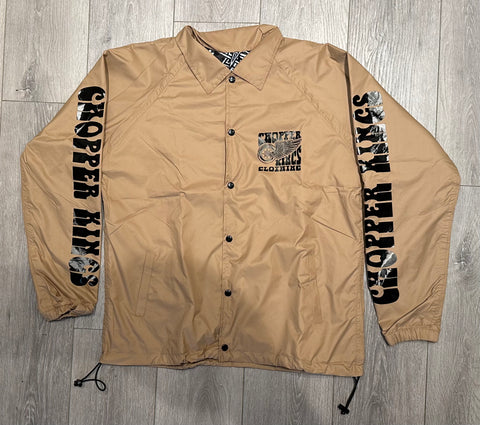 Beige jacket with black text and graphics on sleeves and chest, displayed on a wooden floor.