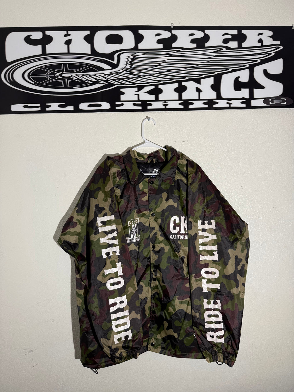 Camouflage jacket with 'Ride to Live' text next to a 'Topper Cloths' logo on a white background