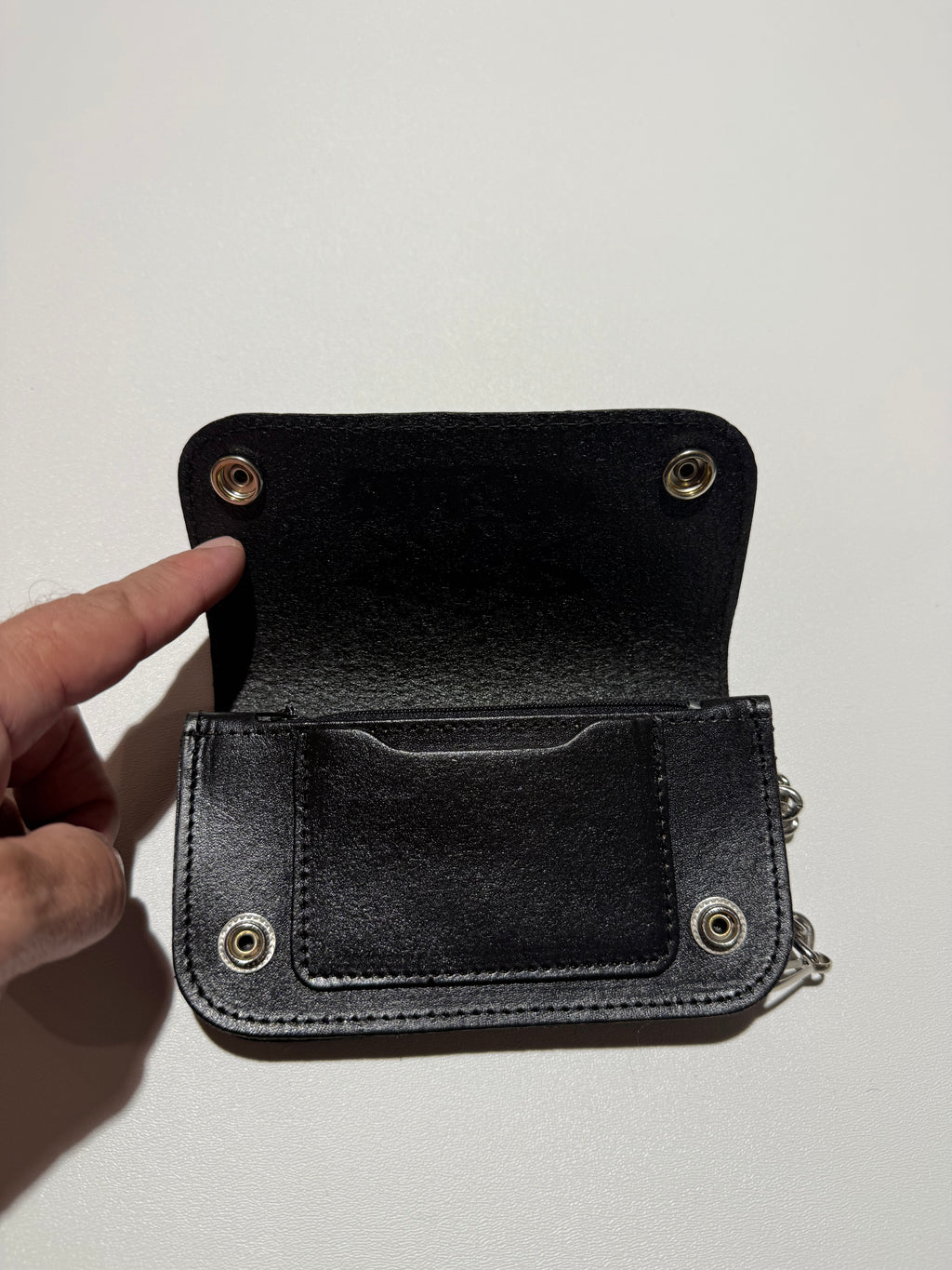 Black leather wallet with metal grommets held open by a hand on a light background