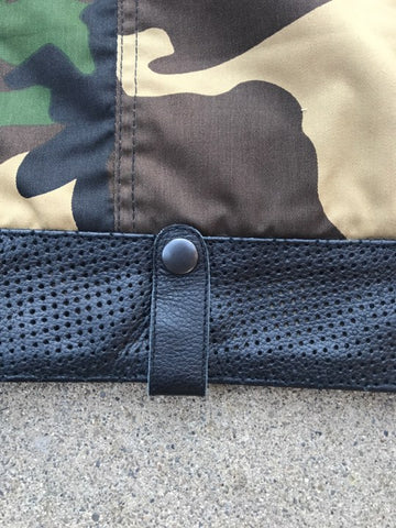 Close-up of a camouflage-patterned fabric with a button and perforated leather on a neutral background